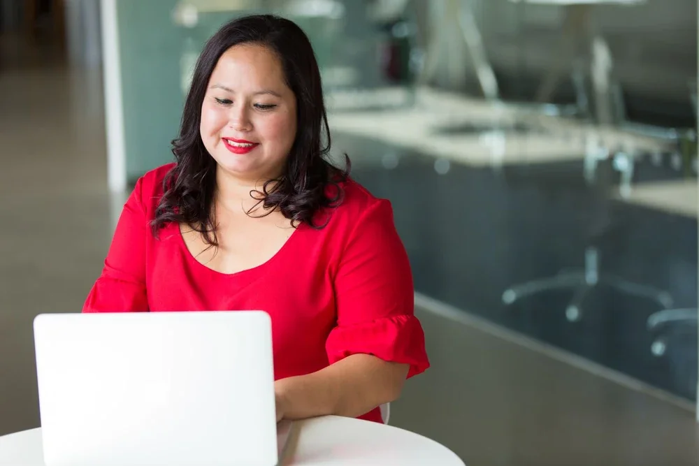 Woman in a red blouse working on a laptop at her desk